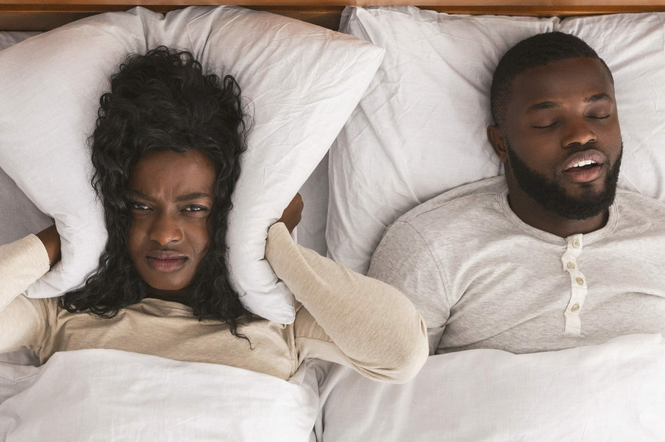 Woman covers ears as man snored in bed next to her.