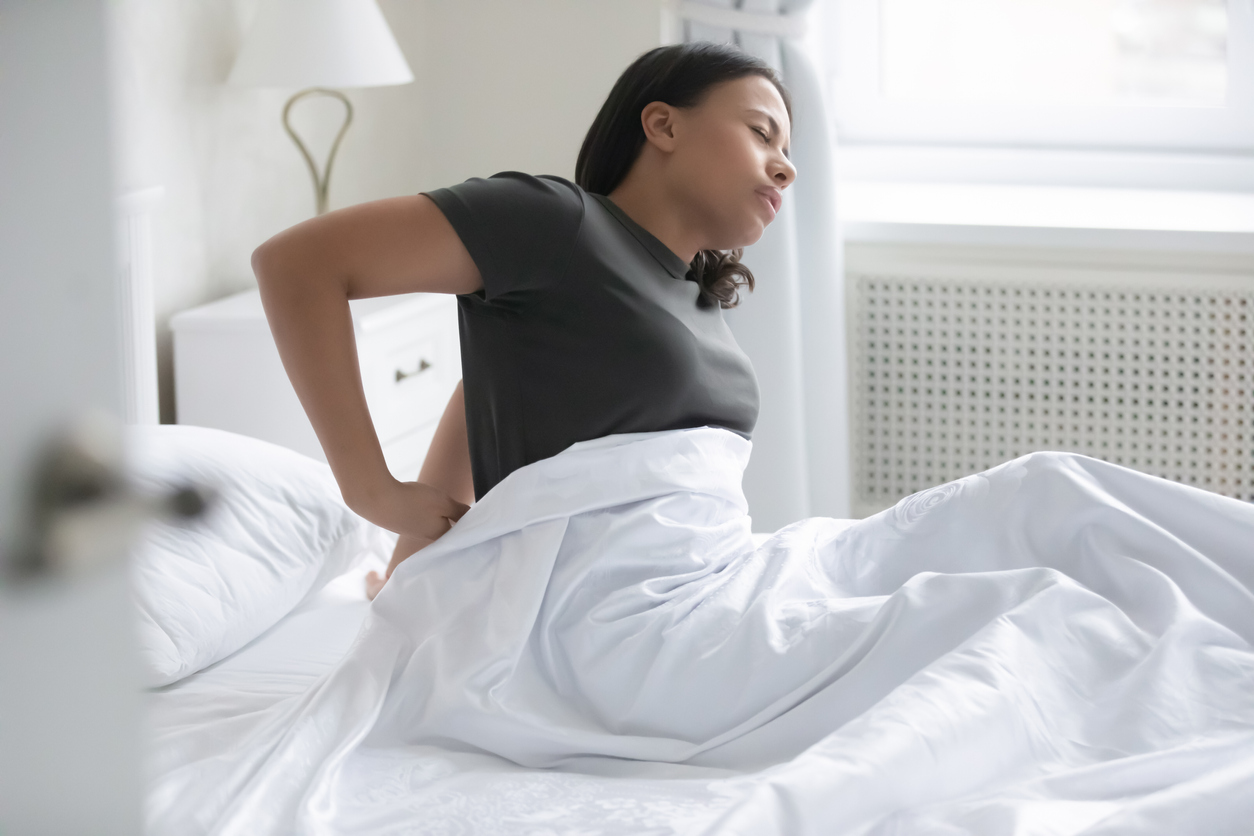 A woman sitting up in bed with low back pain. Finding the right pregnancy sleeping positions can help you sleep comfortably right the way through your pregnancy.